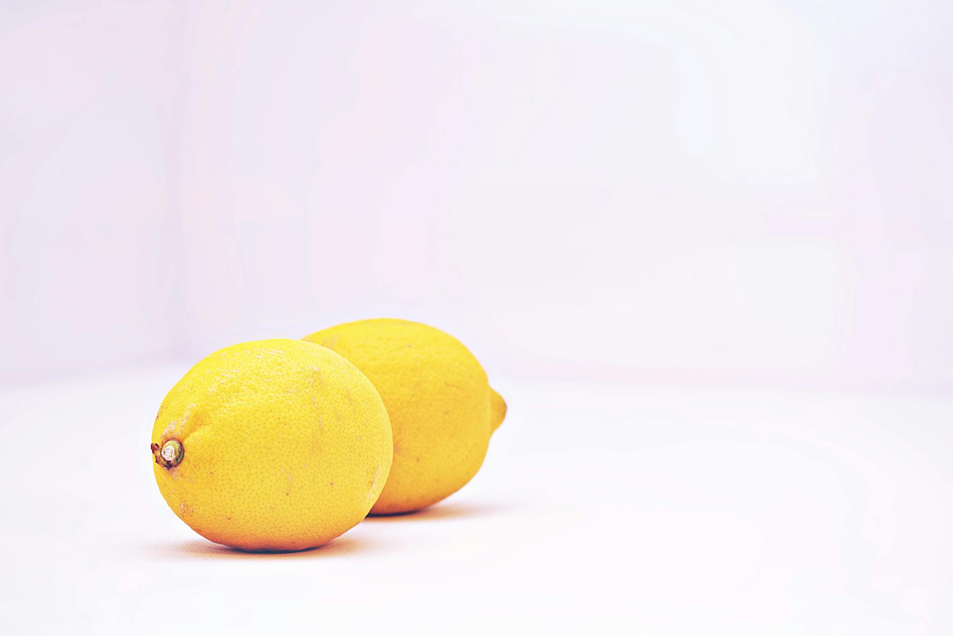 A hand holding a lemon on soft pink background with additional lemons nearby, representing fresh sensations and renewed pleasure.