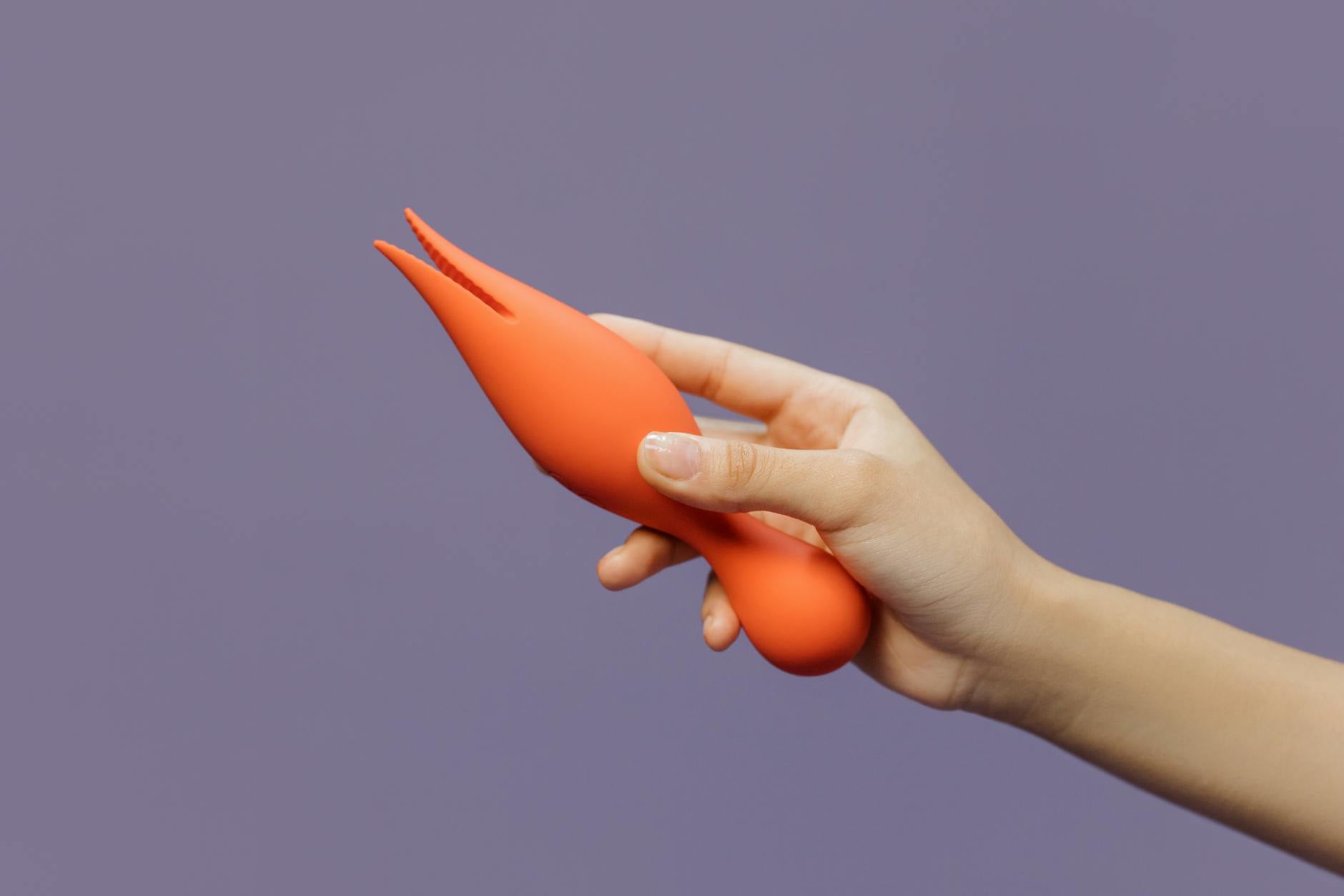 Hand holding a bright yellow clitoral vibrator against a minimalist purple backdrop, representing modern couples' intimacy.