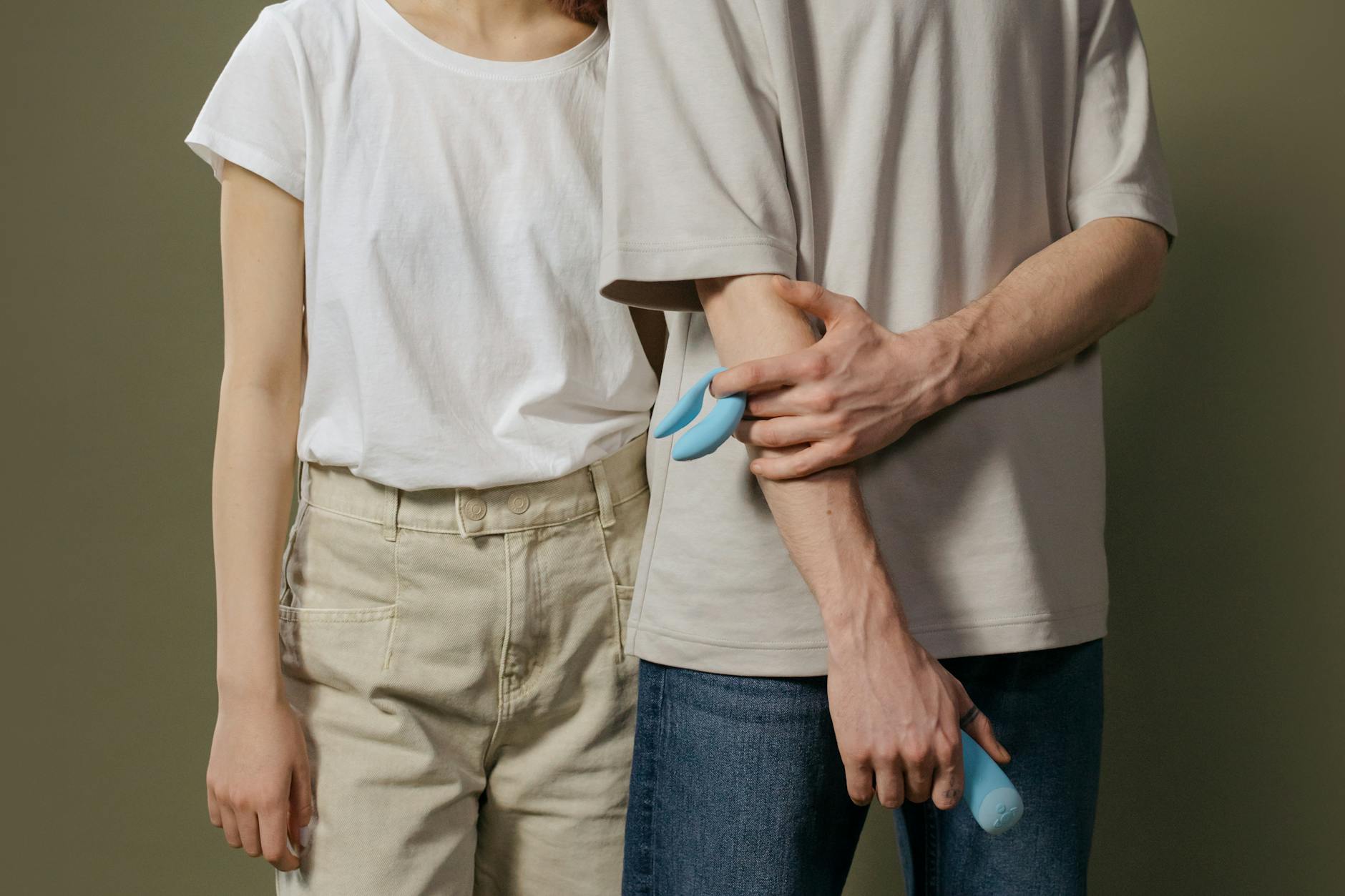 A young couple standing together indoors, holding a blue vibrator, symbolizing modern intimacy and communication about pleasure.