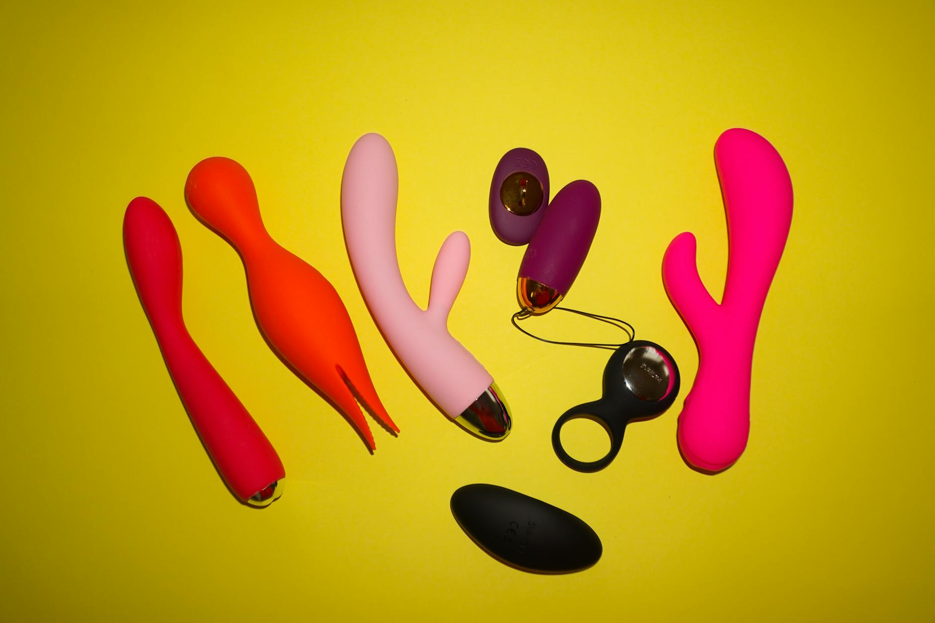Colorful clitoral vibrators and lemon sucker toys arranged on a bright yellow surface